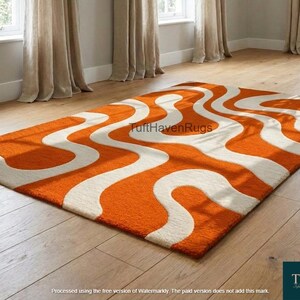 May include: An orange and white wavy pattern rug on a hardwood floor. The rug is rectangular and features a bold, retro design. The room has neutral-colored walls, beige curtains, and natural light from the windows.