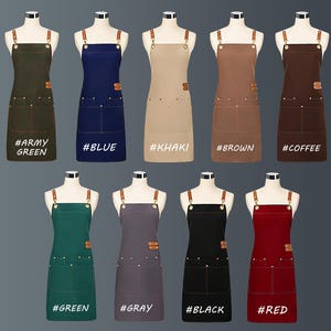 May include: A selection of aprons in shades such as army green, blue, khaki, brown, coffee, green, grey, black, and red. Each apron features a bib, two front pockets, and leather straps. The aprons are displayed on mannequins.