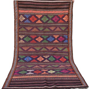 May include: A rectangular woven rug featuring a dark purple base with horizontal bands of geometric patterns. The design includes rows of diamonds in blue, green, orange, and magenta, separated by thin striped borders and a Greek key edge trim.