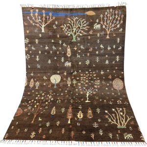 Könnte beinhalten: Ein großer, rechteckiger brauner Teppich mit einem detaillierten Muster aus Bäumen, Tieren und floralen Motiven. Das Design weist verschiedene Farben auf, darunter Blau, Grün und Gelb, was einen lebendigen und künstlerischen Look erzeugt. Der Teppich hat einen Fransenrand.