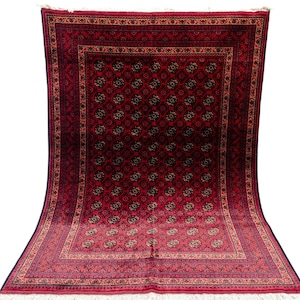 May include: A large, rectangular red rug with an intricate floral pattern. The rug features a central field of repeating floral medallions in black and gold, framed by a detailed border. The rug has a fringe along the edges.