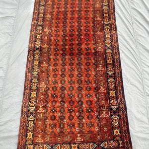 May include: A rectangular area rug featuring a vibrant red field with a repeating geometric lattice pattern in black and white. The rug is framed by multiple decorative borders in navy blue, red, and yellow, finished with short white fringe at ends.