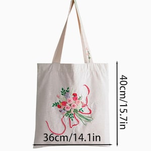 May include: Cream-colored tote bag with embroidered floral design. The bag features a bouquet of pink, red, and purple flowers with green leaves and red ribbons. The bag is 14.1 inches wide and 15.7 inches tall.