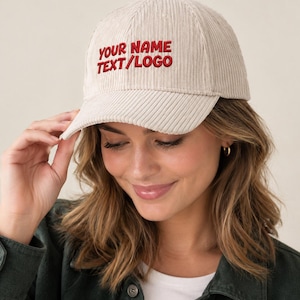 May include: A beige corduroy baseball cap featuring the embroidered red text YOUR NAME TEXT/LOGO on the front panel. The cap has a structured crown, a curved brim, and a button on top, showcasing a textured fabric finish throughout the design.