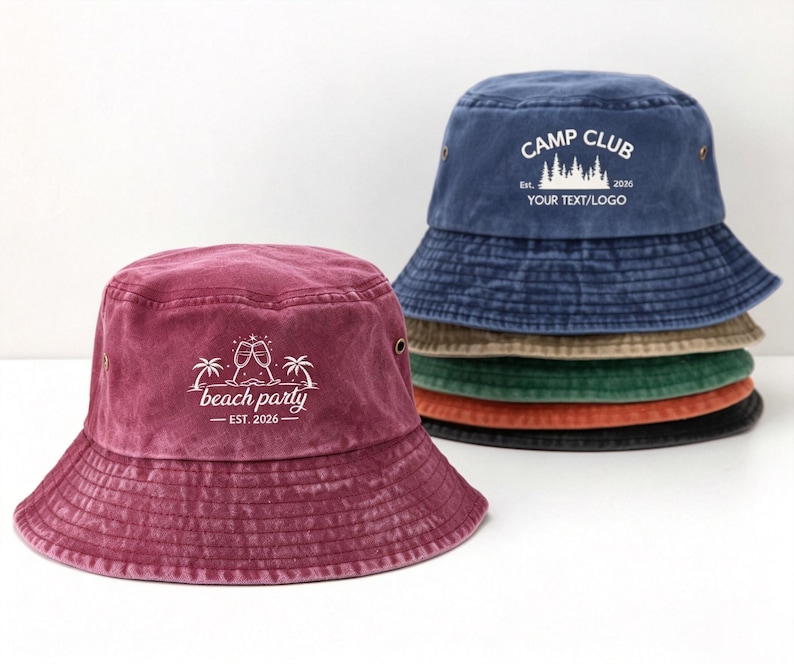 May include: A stack of five cotton bucket hats in maroon, blue, tan, green, orange, and black. The top blue hat features white text reading CAMP CLUB EST. 2026 YOUR TEXT/LOGO. The front maroon hat displays white text reading beach party EST. 2026.