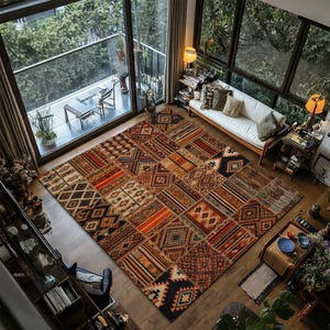 May include: A large, rectangular area rug with a patchwork design. The rug features a variety of geometric and striped patterns in shades of brown, orange, and beige. The rug is placed on a wooden floor in a living room setting.