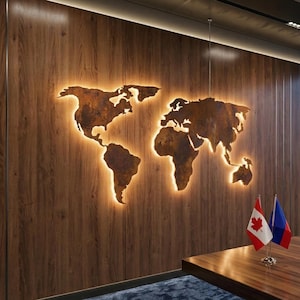 May include: A metal world map, illuminated from behind, mounted on a wooden wall. The map is a rusty brown colour, with a warm, orange glow. Two small flags are on a wooden table in the foreground.