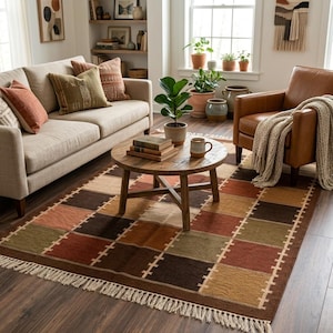 May include: A rectangular rug with a patchwork design in shades of brown, orange, and green. The rug has a fringe along the edges and is placed on a wooden floor. A round wooden coffee table sits on the rug.