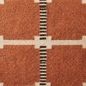 May include: A woven textile featuring a grid pattern of large burnt orange squares separated by thin white horizontal lines and vertical bands composed of alternating thin black and white stripes that intersect at the center of the grid.