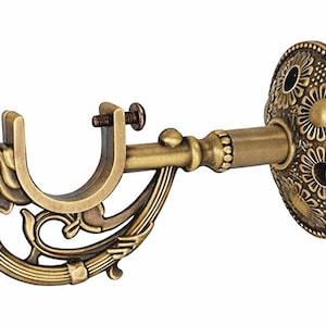 May include: An antique-style curtain rod bracket in a brass finish. The bracket has a U-shaped holder, a decorative support arm, and a circular wall plate with embossed floral patterns. The bracket is designed for a curtain rod.