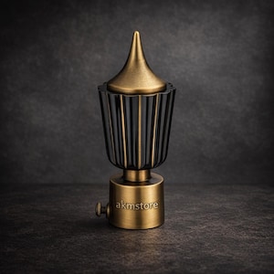 Puede incluir: Un terminal decorativo para barra de cortina, con una parte superior cónica dorada y un cuerpo negro acanalado. La base cilíndrica es dorada y lleva grabado el texto "akmstore". Diseñado para cortinas, añade un toque de elegancia.