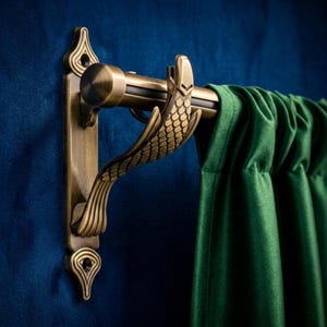 Może przedstawiać: Mosiężny karnisz z dekoracyjnymi detalami w kształcie łusek ryb i pasującym wspornikiem. Karnisz trzyma zieloną aksamitną zasłonę na niebieskiej ścianie. Design karnisza dodaje elegancji wystrojowi pokoju.