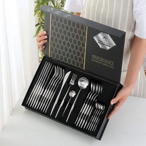 Puede incluir: Un juego de cubiertos pulidos de alta calidad presentado en una caja negra. El juego incluye tenedores, cuchillos, cucharas y cucharas de servir. La caja tiene un patrón geométrico y el texto "HIGH QUALITY Polished Cutlery Set".