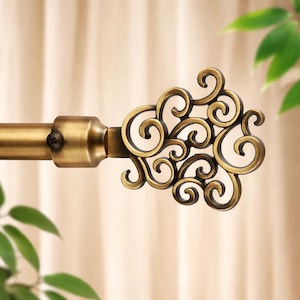 May include: A decorative bronze-colored curtain rod with an ornate, swirling finial. The rod and its hardware have a vintage aesthetic, with a warm, metallic finish. The finial features intricate scrollwork, adding a touch of elegance to the window treatment.