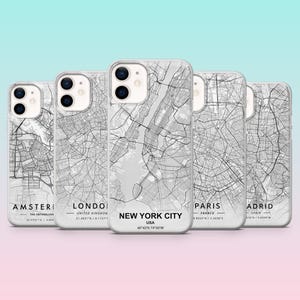 Op de afbeelding: Een verzameling telefoonhoesjes met gedetailleerde zwart-wit stadsplattegronden. De hoesjes tonen kaarten van Amsterdam, Londen, New York City, Parijs en Madrid. Op elke hoes staat de naam van de stad en de coördinaten.
