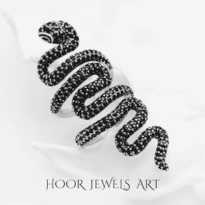 Könnte beinhalten: Ein silberner Schlangenring mit schwarzen Steinen. Das Design zeigt eine sich windende Schlange mit detailliertem Kopf und Körper. Der Ring ist vor weißem Hintergrund platziert. Der Text "HOOR JEWELS ART" ist zu sehen.