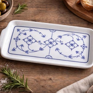May include: A rectangular white ceramic serving tray with a blue floral design. The tray has two handles and is surrounded by olives, rosemary, and bread. The blue pattern is symmetrical and decorative.