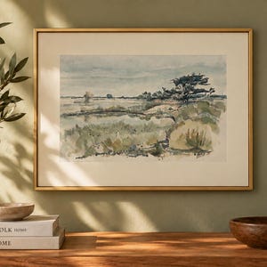 Puede incluir: Un cuadro de paisaje rectangular en un marco dorado fino que presenta una escena de acuarela de un campo pantanoso con tonos apagados de verde, azul y marrón, un árbol oscuro a la derecha y un cielo pálido, exhibido con un amplio paspartú color crema.