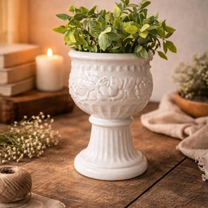 Maceta vintage de cerámica blanca con pedestal, con relieve floral, estilo mediados de siglo.