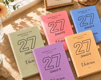 Può includere: Cinque quaderni rettangolari di colore verde chiaro, rosa, blu, viola e arancione. Ogni copertina riporta il testo "MEMORIES IN THE MAKING", il numero "27", la parola "senior" e un nome come "Victoria" stampati in nero.