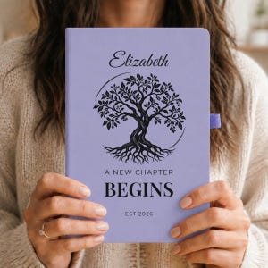 May include: A light purple notebook featuring a black graphic of a tree with roots, the name Elizabeth, and the text A NEW CHAPTER BEGINS EST 2026. The notebook has a matching purple elastic pen loop on the right side of the cover.