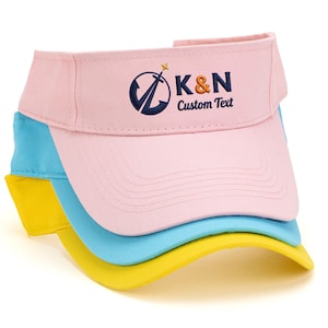 May include: Three visors stacked, each in a different color: pink, light blue, and yellow. The top pink visor has a logo with the letters "K&N" and the words "Custom Text". The visors are made of a soft fabric.
