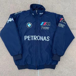 May include: Navy blue zip-up jacket with the BMW logo and "PETRONAS" printed in white. The jacket features "M Power" and "Credit Suisse" branding. The jacket has a stand-up collar and black ribbed cuffs and hem.