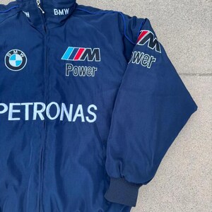 May include: Navy blue BMW Petronas jacket with a high collar and a zipper closure. The jacket features the BMW logo, the words "BMW", "Power", and "Petronas" in white, red, and blue. The sleeves have black cuffs.
