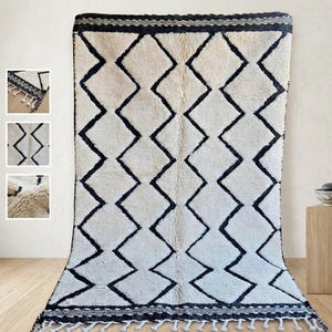 May include: A large, rectangular rug with a cream-colored background and a repeating pattern of black diamond shapes. The rug has a black border and fringe along the bottom edge. The rug is made of a thick, textured material.