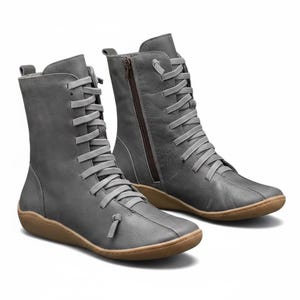 K&ouml;nnte beinhalten: Ein Paar graue Lederstiefel mit Schn&uuml;rung und seitlichem Rei&szlig;verschluss. Die Stiefel haben eine runde Spitze und eine braune Sohle. Die Stiefel sind etwa 20 cm hoch.