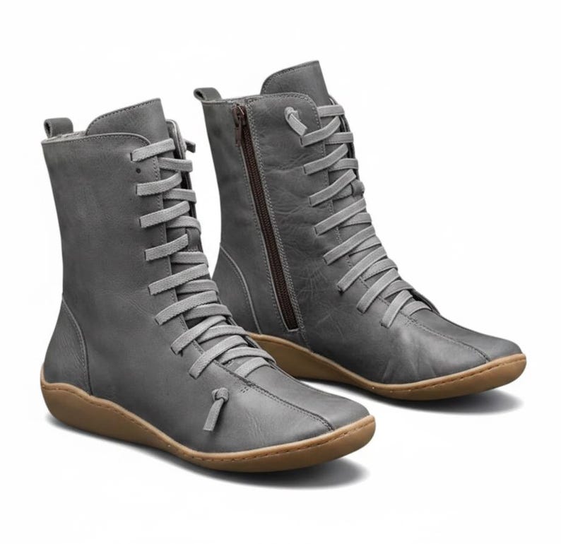 K&ouml;nnte beinhalten: Ein Paar graue Lederstiefel mit Schn&uuml;rung und seitlichem Rei&szlig;verschluss. Die Stiefel haben eine runde Spitze und eine braune Sohle. Die Stiefel sind etwa 20 cm hoch.