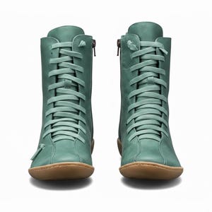 K&ouml;nnte beinhalten: Ein Paar tealfarbene kn&ouml;chelhohe Stiefel mit Schn&uuml;rung und seitlichen Rei&szlig;verschl&uuml;ssen. Die Stiefel haben eine runde Spitze und eine braune Sohle. Die Schn&uuml;rsenkel und das Leder sind gleichfarbig. Vor wei&szlig;em Hintergrund.