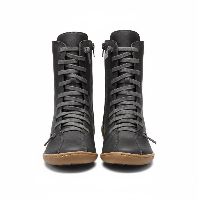 K&ouml;nnte beinhalten: Ein Paar dunkelgraue Lederstiefel mit grauen Schn&uuml;rsenkeln und einem seitlichen Rei&szlig;verschluss. Die Stiefel haben eine runde Spitze und eine braune Sohle. Die Stiefel sind kniehoch.