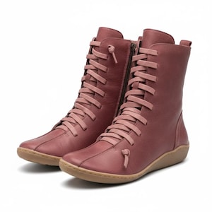 K&ouml;nnte beinhalten: Ein Paar staubrosafarbene kniehohe Stiefel. Die Stiefel haben ein Schn&uuml;rdesign mit passenden Schn&uuml;rsenkeln, einen seitlichen Rei&szlig;verschluss und eine runde Spitze. Die Sohlen sind hellbraun.
