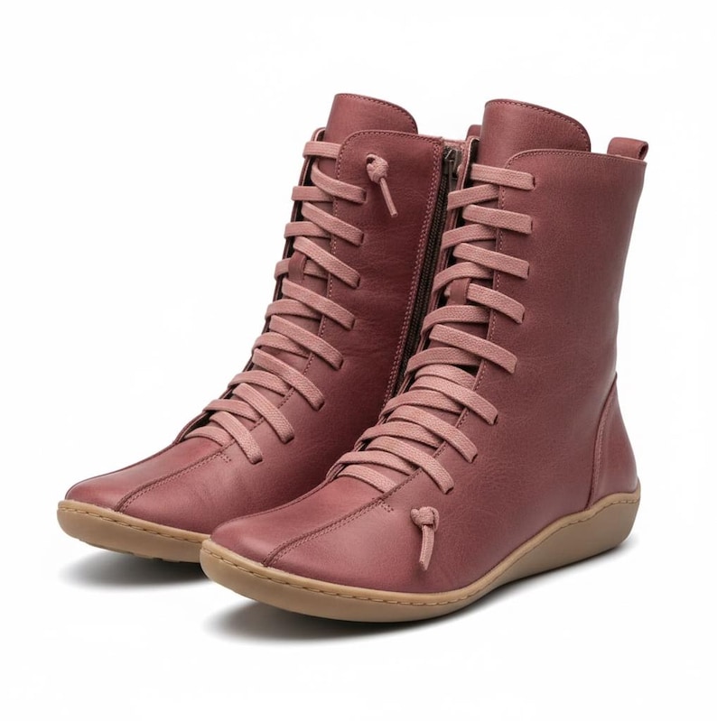 K&ouml;nnte beinhalten: Ein Paar staubrosafarbene kniehohe Stiefel. Die Stiefel haben ein Schn&uuml;rdesign mit passenden Schn&uuml;rsenkeln, einen seitlichen Rei&szlig;verschluss und eine runde Spitze. Die Sohlen sind hellbraun.