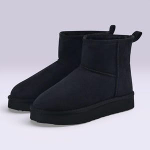 Könnte beinhalten: Ein Paar schwarze Stiefeletten mit runder Spitze und dicker Sohle. Die Stiefel haben eine weiche, Wildleder-ähnliche Textur und einen kurzen Schaft. Am oberen Rand des Stiefels ist eine kleine Schlaufe befestigt.