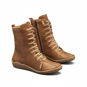 K&ouml;nnte beinhalten: Ein Paar braune Lederstiefel mit Schn&uuml;rung und seitlichem Rei&szlig;verschluss. Die Stiefel haben eine flache Sohle und eine runde Spitze. Die Schn&uuml;rsenkel und der Rei&szlig;verschluss sind heller als die Stiefel selbst.