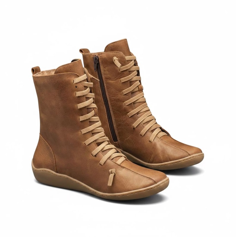 K&ouml;nnte beinhalten: Ein Paar braune Lederstiefel mit Schn&uuml;rung und seitlichem Rei&szlig;verschluss. Die Stiefel haben eine flache Sohle und eine runde Spitze. Die Schn&uuml;rsenkel und der Rei&szlig;verschluss sind heller als die Stiefel selbst.