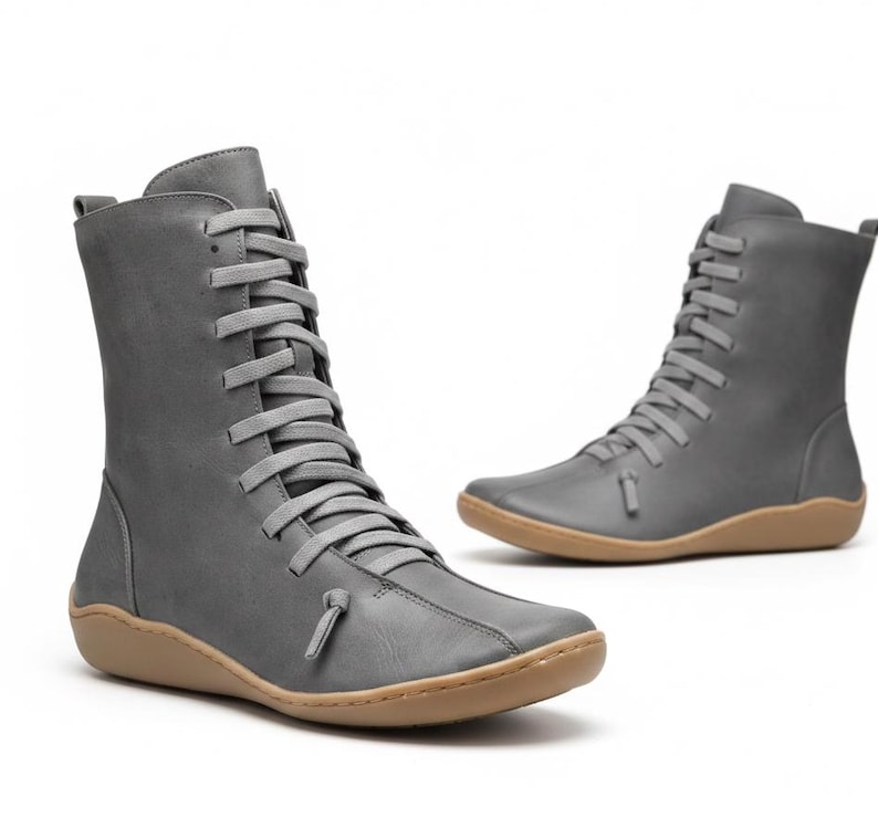 K&ouml;nnte beinhalten: Zwei graue Lederstiefel mit hellbraunen Sohlen. Die Stiefel haben eine mittlere Wadenh&ouml;he und sind vorne mit grauen Schn&uuml;rsenkeln geschn&uuml;rt. Das Design ist minimalistisch und modern, passend f&uuml;r verschiedene Outfits.