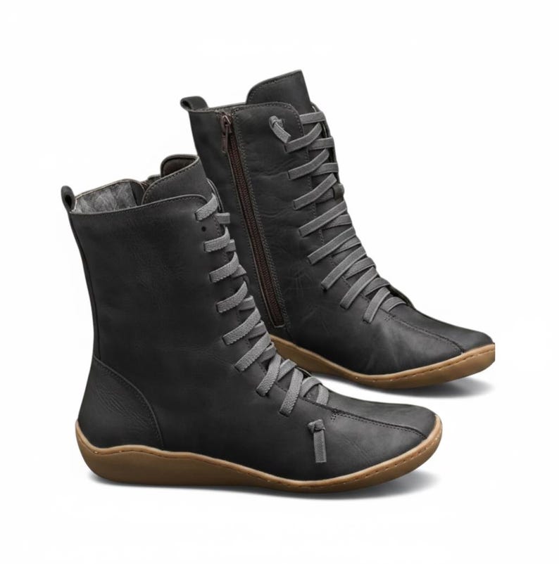 K&ouml;nnte beinhalten: Ein Paar schwarze kn&ouml;chelhohe Stiefel mit grauen Schn&uuml;rsenkeln und braunen Sohlen. Ein Stiefel hat einen seitlichen Rei&szlig;verschluss. Die Stiefel haben eine runde Spitze und ein l&auml;ssiges Design, das f&uuml;r den Alltag geeignet ist. Die Schn&uuml;rsenkel sind durch Metall&ouml;sen gef&auml;delt.