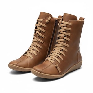 K&ouml;nnte beinhalten: Ein Paar braune Lederstiefel mit beigen Schn&uuml;rsenkeln und einem seitlichen Rei&szlig;verschluss. Die Stiefel haben eine runde Spitze und eine flache Sohle. Die Stiefel sind kniehoch.