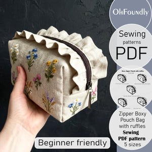 Può includere: Un astuccio con cerniera a forma di scatola beige con ricami floreali e una parte superiore a balze. L'astuccio ha una cerniera marrone e un piccolo tirante. È visibile anche il testo "Beginner friendly" e "Sewing patterns PDF".