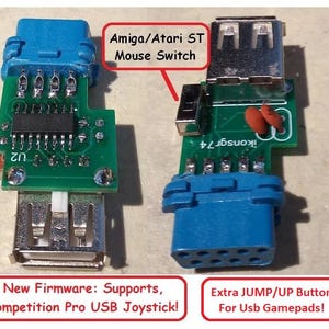 May include: Two green circuit boards with blue connectors and USB ports. Text on the boards reads "Amiga/Atari ST Mouse Switch", "New Firmware: Supports, Competition Pro USB Joystick!", and "Extra JUMP/UP Button For Usb Gamepads!"