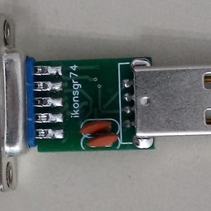 May include: A silver USB to serial adapter with a DB9 connector. The adapter has a green circuit board with the text "ikonsgr74". The USB connector is rectangular with two openings.