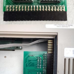 May include: A green circuit board labelled "512Kb Ram Expansion" for Amiga 500 computers. The board features electronic components, including chips and connectors. A second green circuit board is visible inside a computer case.