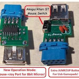 May include: A green circuit board adapter featuring a blue 9-pin connector and a silver USB port. Text on the board reads 'ikonsgr74'. Labels include 'Amiga/Atari ST Mouse Switch', 'New Operation Mode: Mouse->Joy Port for 8bit Micros!', and 'Extra JUMP/UP Button For Usb Gamepads!'