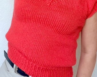 May include: A vibrant red knitted top with a V-neck design. The short-sleeved top has a ribbed hem and a fitted silhouette. The top is paired with light-colored pants and a black belt with a silver buckle.