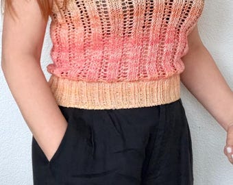 May include: A knitted top in shades of peach and coral, with a square neckline and a ribbed hem. The top is paired with black pants. The knitted top is a sleeveless design.