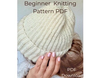 May include: A cream-colored ribbed knit beanie with a folded brim. The text "Beginner Knitting Pattern PDF" is printed at the top, and "PDF Download" is printed at the bottom right of the image.