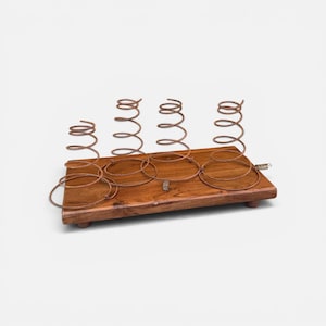 May include: A rectangular wooden base with a natural brown finish, featuring four upright, conical metal springs attached to the surface. The springs are arranged in a row, and the entire structure is supported by small, rounded wooden feet.